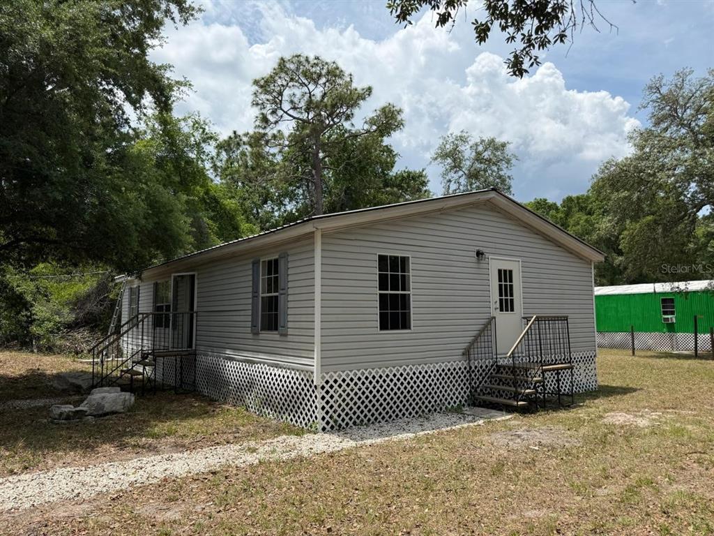 A light gray manufactured home with white lattice skirting and metal stairs sits outdoors — 10405 JUNGLE STREET, NEW PORT RICHEY, FL