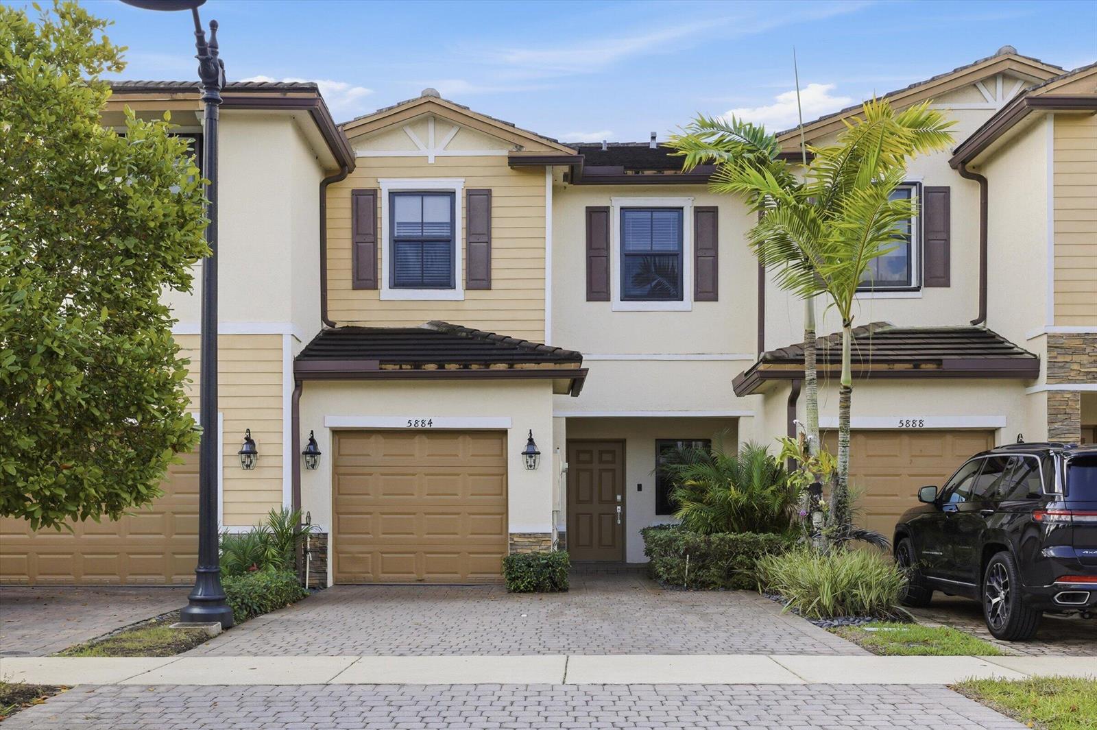 A two-story townhouse exterior features a tan facade, brown garage doors, and a paved driveway — 5884 Mustang Manor, Davie FL 33314, DAVIE, FL