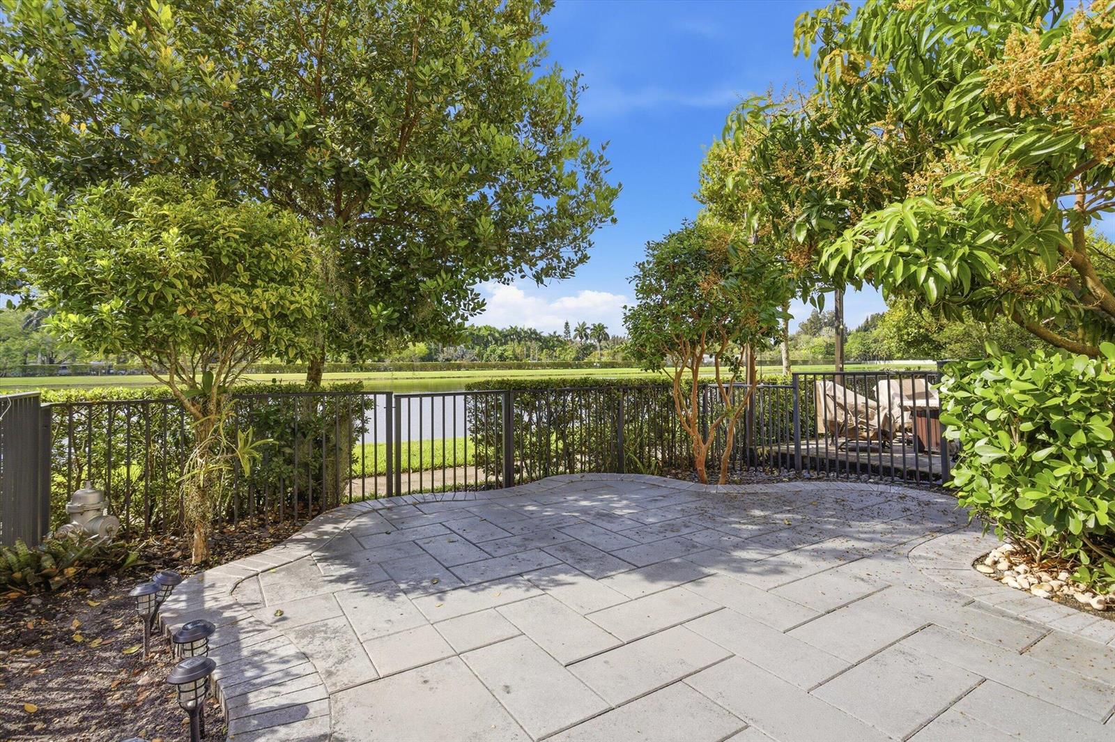A paved patio overlooks a lake and green space behind a metal fence — 5884 Mustang Manor, Davie FL 33314, DAVIE, FL