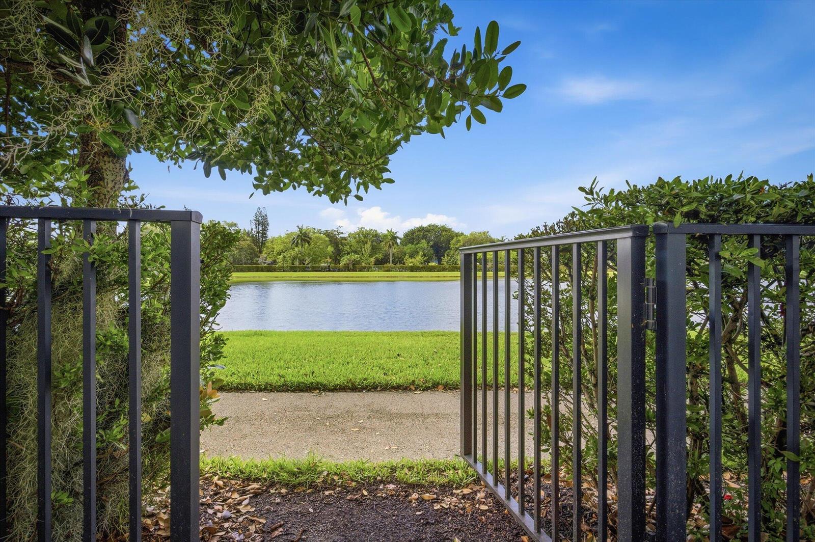 A black metal gate opens to a view of a grassy lawn and a lake — 5884 Mustang Manor, Davie FL 33314, DAVIE, FL