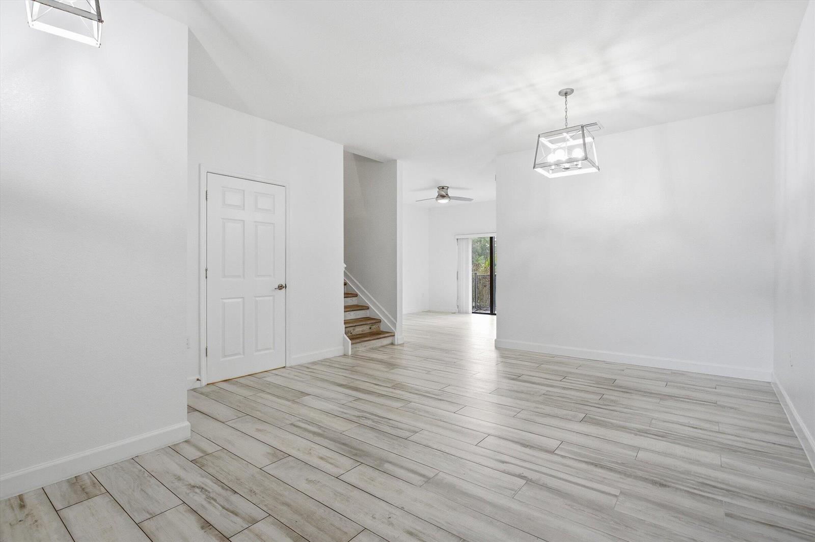 A bright, empty room features light wood-look tile flooring, a white door, and a chandelier — 5884 Mustang Manor, Davie FL 33314, DAVIE, FL