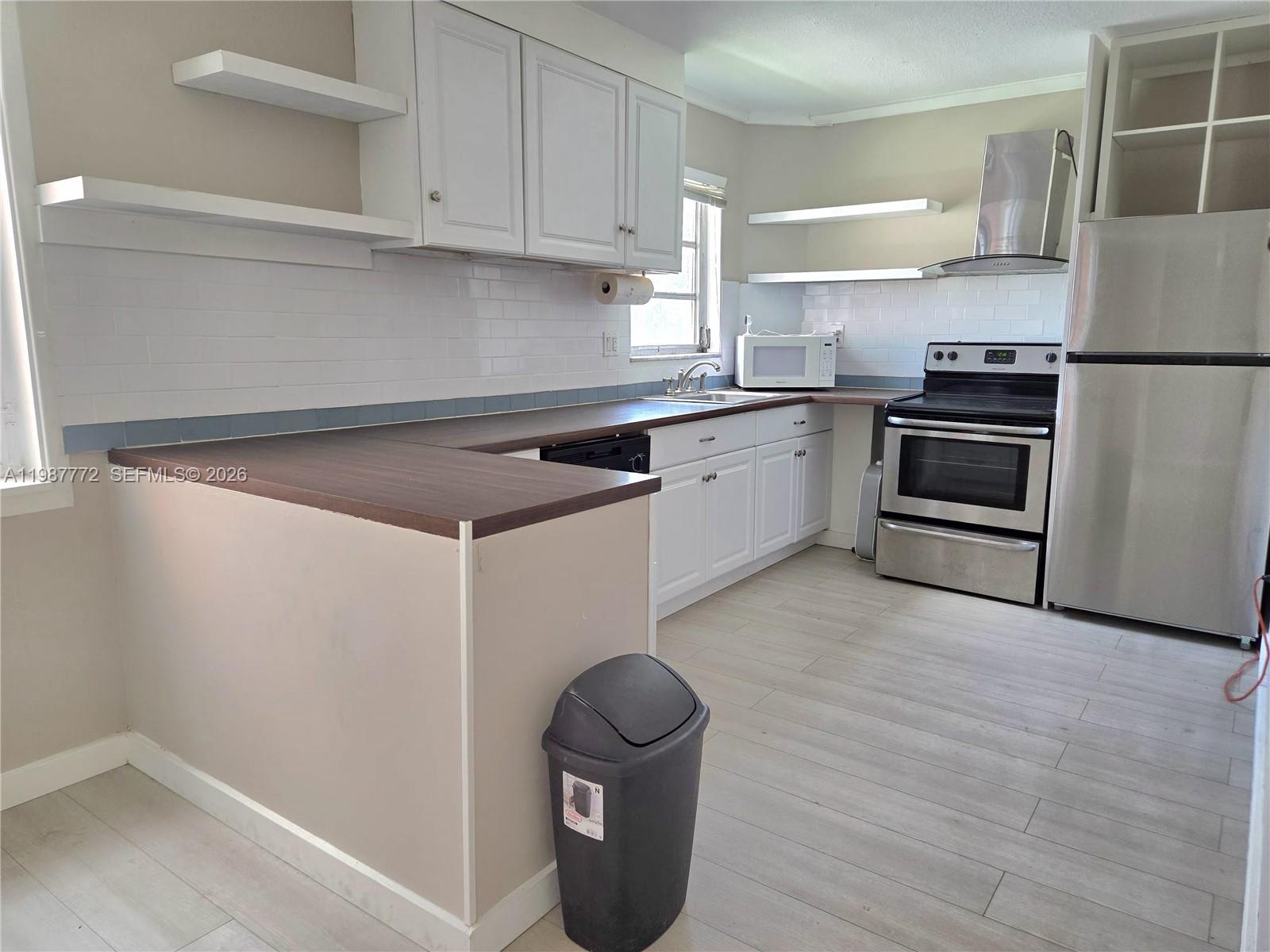 A kitchen features white cabinets, dark wood countertops, stainless steel appliances, and light-colored flooring — 1700 NE 191st St # 100, Miami FL 33179, MIAMI, FL