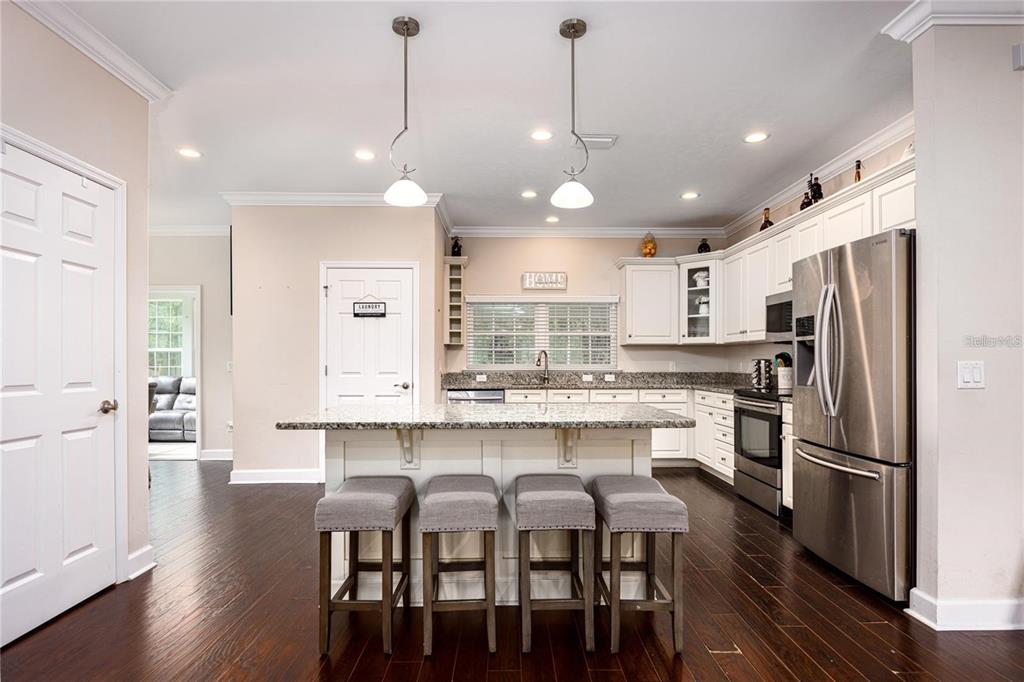 A kitchen features a granite-topped island with four stools, white cabinets, and dark wood floors — 5504 NW 34TH STREET, GAINESVILLE, FL