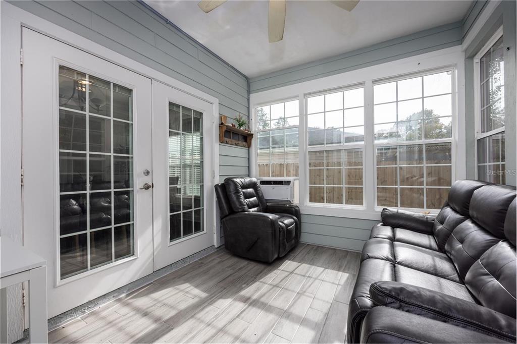 A sunroom features light blue siding, gray wood-look flooring, a black leather sofa, and recliner — 5504 NW 34TH STREET, GAINESVILLE, FL