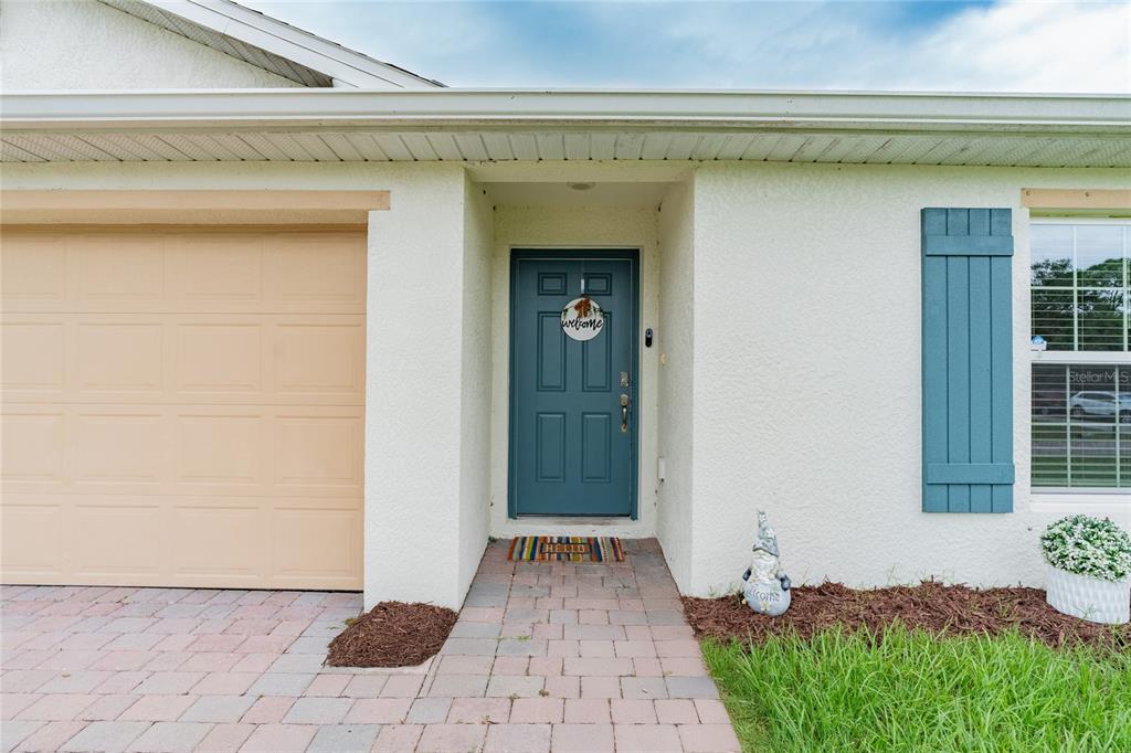The exterior of a house features a beige garage, a blue front door, and shutters — 22420 SACRAMENTO AVENUE, PORT CHARLOTTE, FL