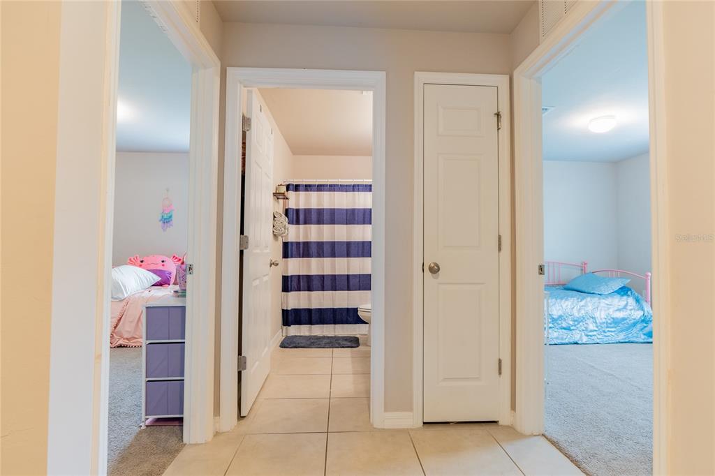 A hallway with tile flooring leads to a bathroom flanked by two bedrooms — 22420 SACRAMENTO AVENUE, PORT CHARLOTTE, FL
