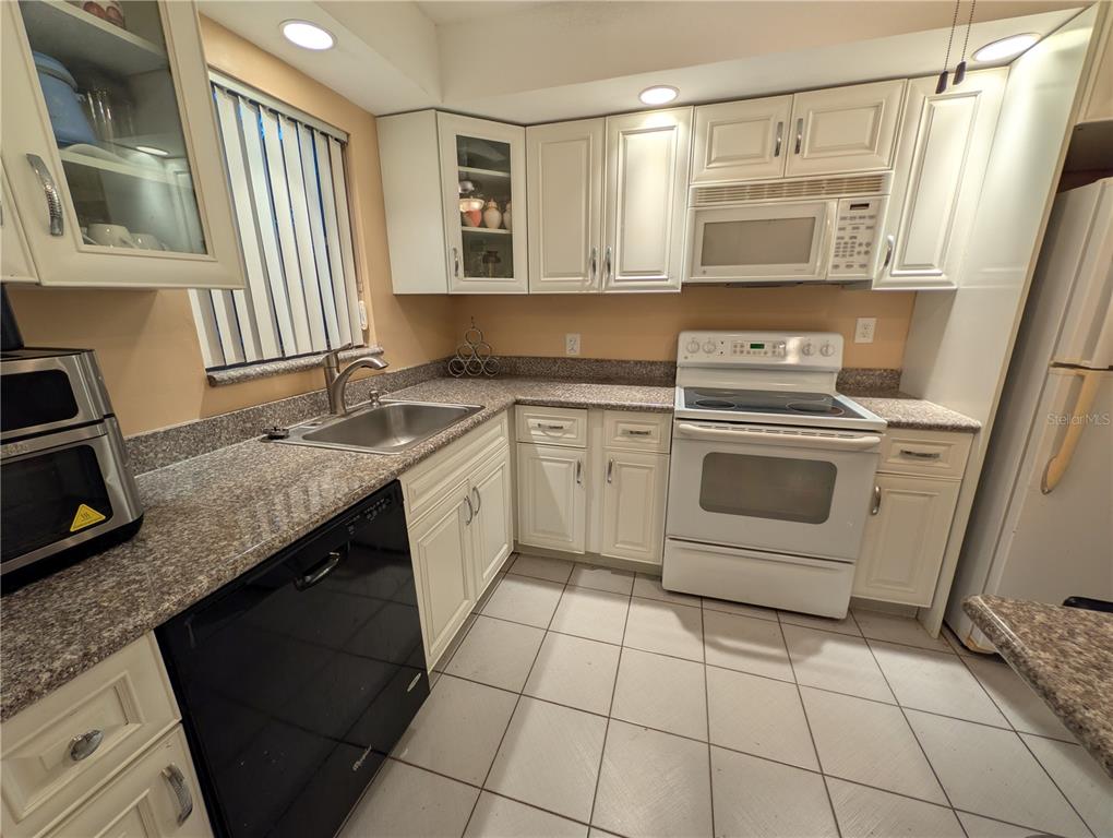 A kitchen features white cabinets, granite countertops, a white stove, and a black dishwasher — 6080 NW 44TH STREET UNIT 301, LAUDERHILL, FL