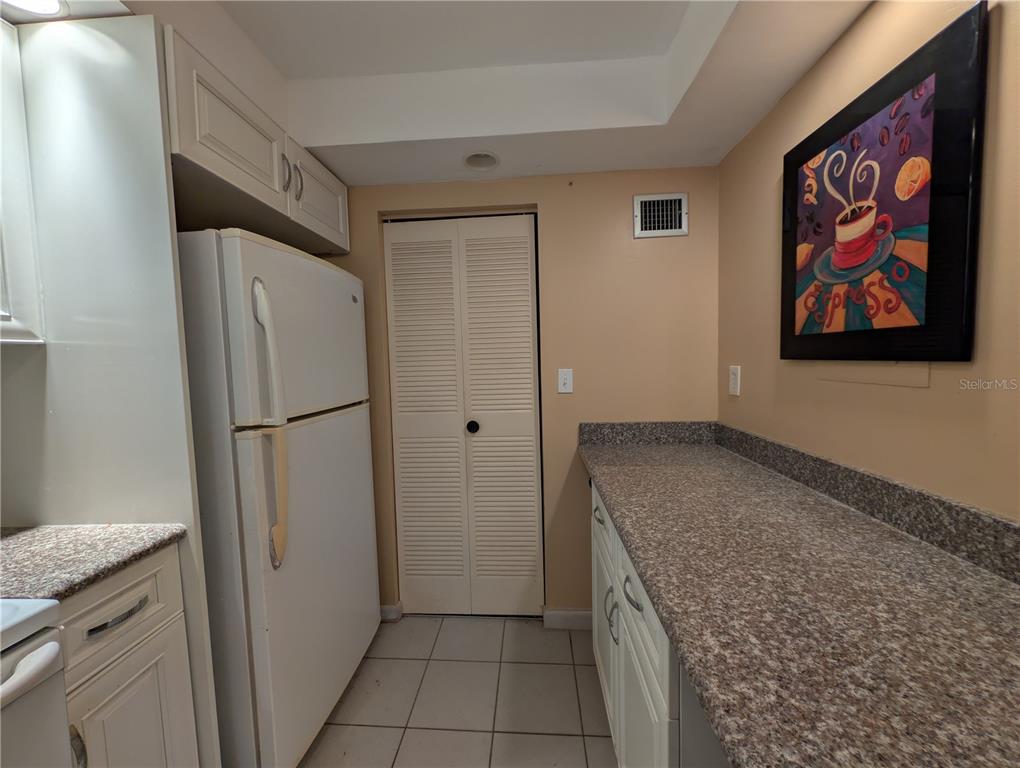 A kitchen features white cabinets, a white refrigerator, granite countertops, and a louvered closet door — 6080 NW 44TH STREET UNIT 301, LAUDERHILL, FL