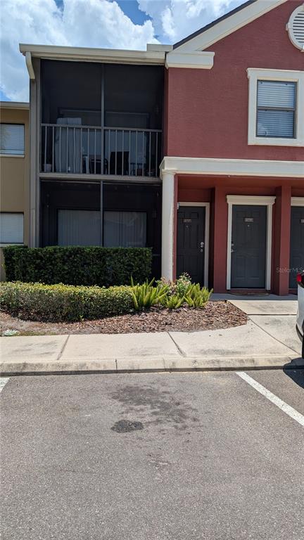 A two-story townhouse exterior features a screened balcony, dark doors, and a landscaped front yard — 5717 BAYWATER DRIVE, TAMPA, FL