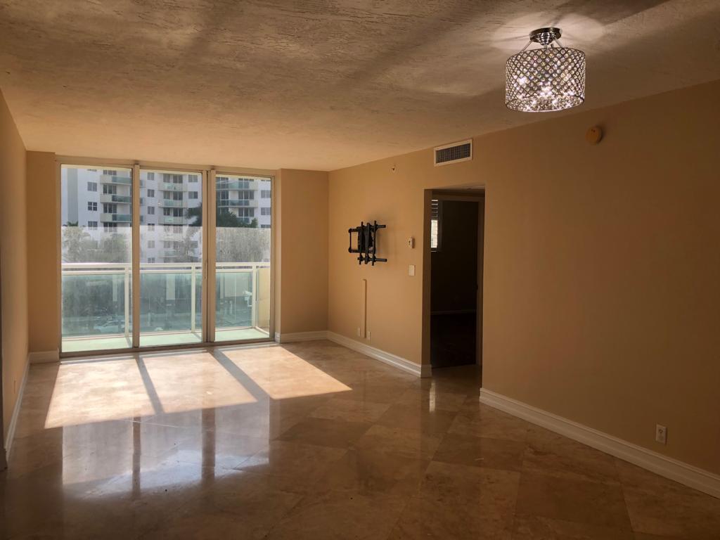An empty living room with beige walls, polished tile floors, a crystal light fixture, and balcony access — 3000 S Ocean Drive # 322, Hollywood FL 33019, HOLLYWOOD, FL