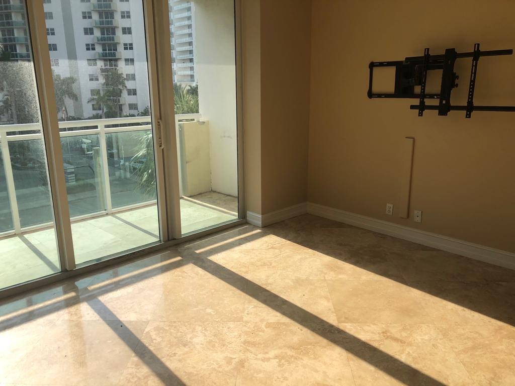 A sunlit room with beige tile flooring, a wall-mounted television bracket, and a sliding glass door — 3000 S Ocean Drive # 322, Hollywood FL 33019, HOLLYWOOD, FL