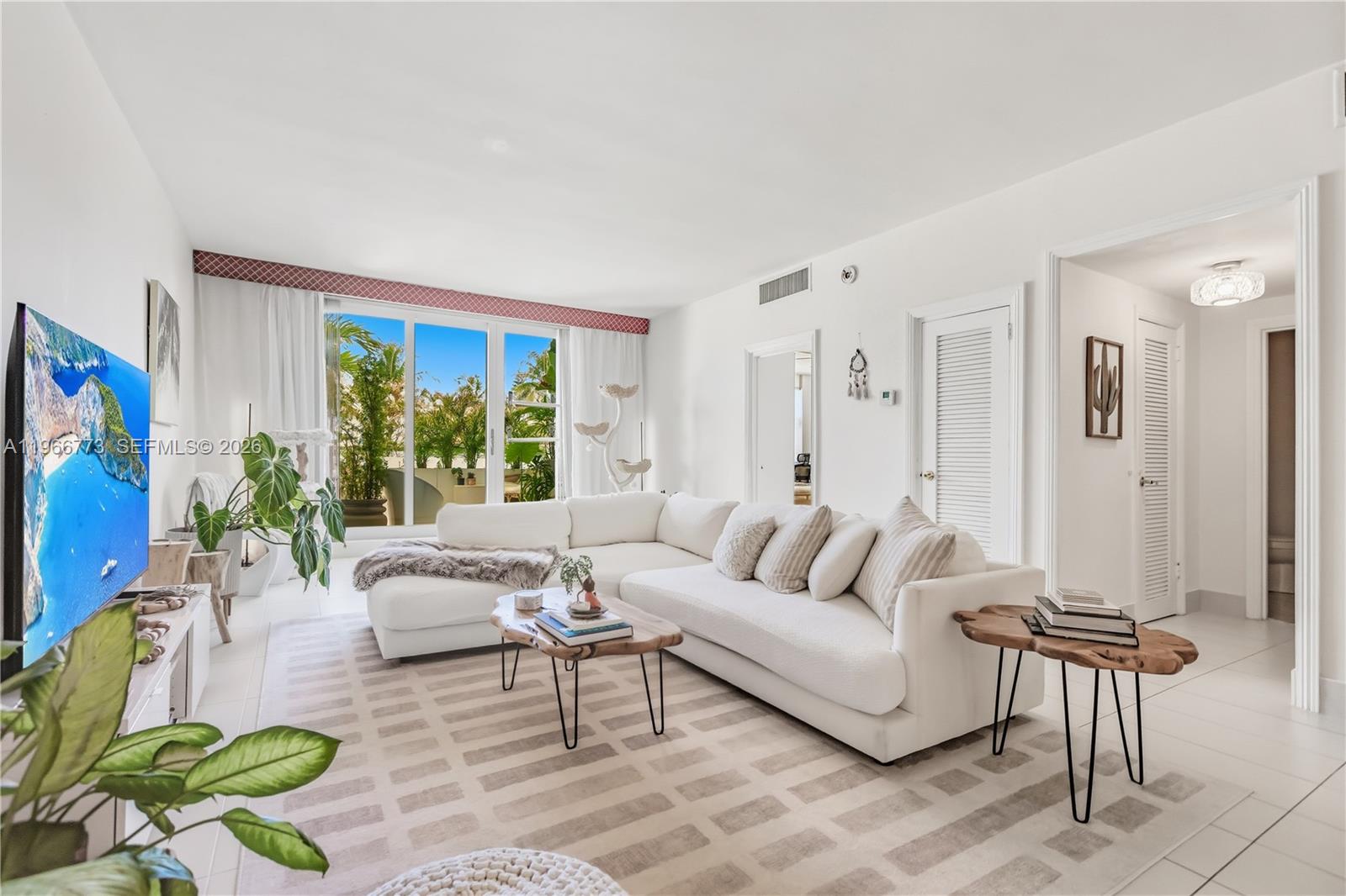 A bright living room features a white sectional sofa, a wooden coffee table, and large windows — 5001 Collins Ave # 1K, Miami Beach FL 33140, MIAMI BEACH, FL