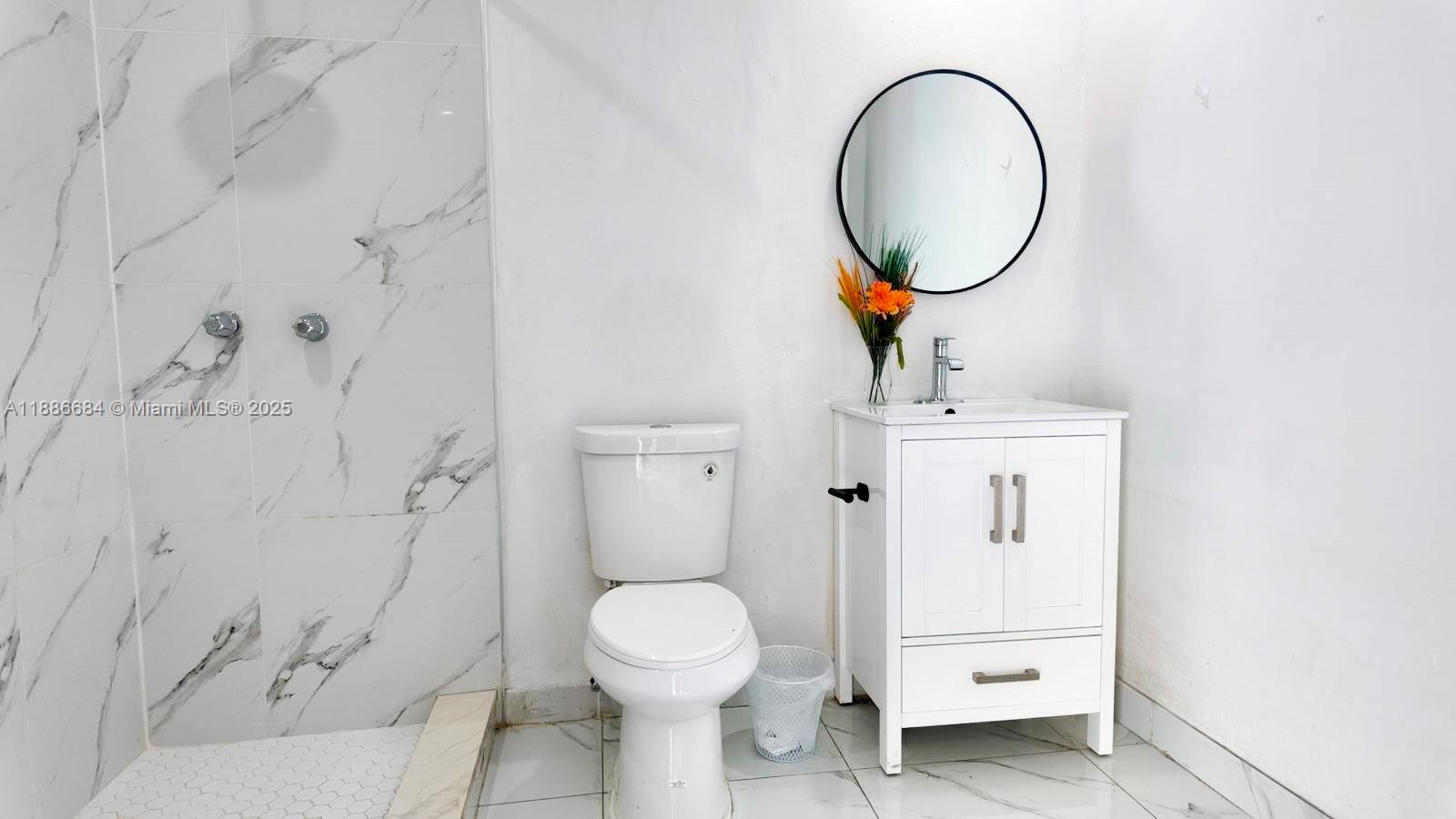 A bathroom features a marble-tiled shower, a white vanity, and a round wall mirror — 2367 NW 82nd St, Miami FL 33147, MIAMI, FL