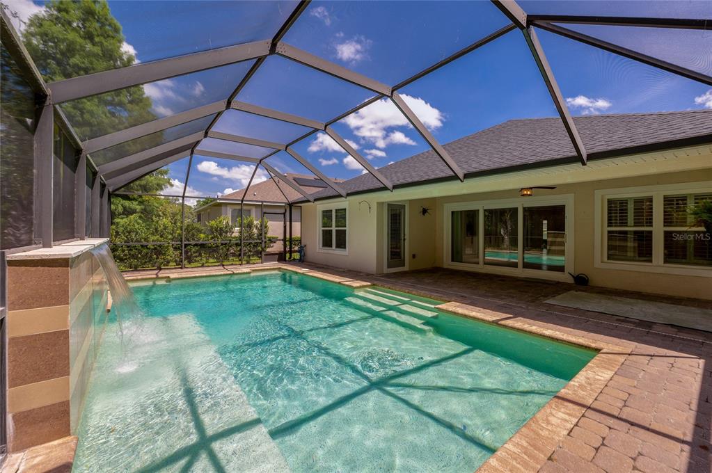 A screened-in swimming pool with a waterfall feature sits on a paved patio behind a house — 312 BIRKDALE DRIVE, DAYTONA BEACH, FL