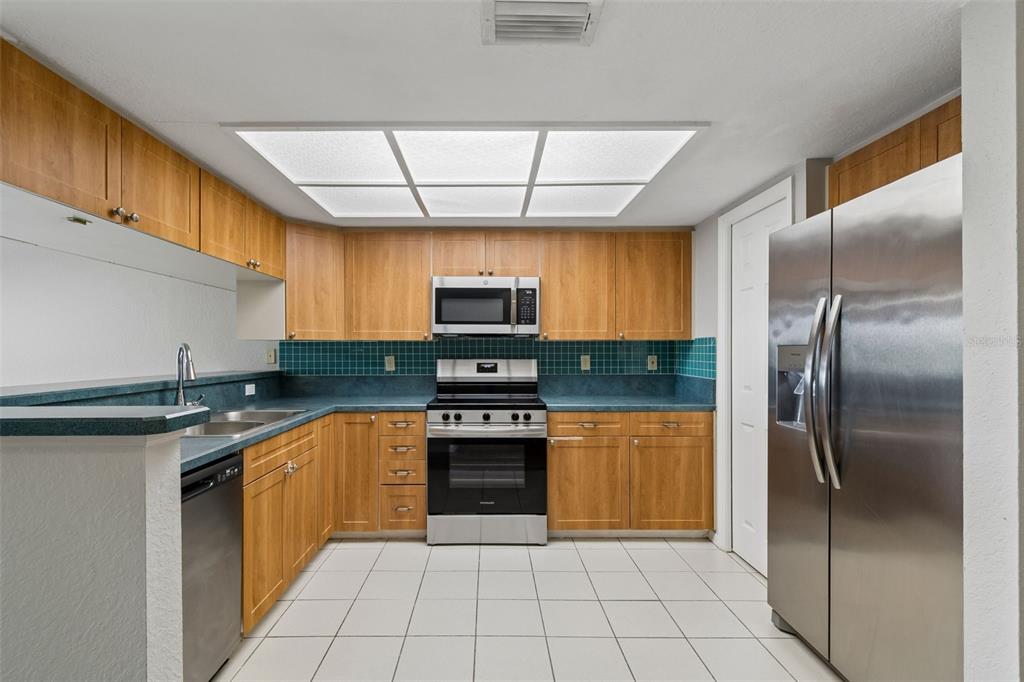 A kitchen features light wood cabinets, teal countertops, stainless steel appliances, and white floor tiles — 14718 SEMINOLE TRAIL, SEMINOLE, FL