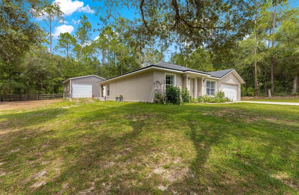 A single-story house with a detached garage sits on a grassy lot surrounded by trees — 1423 W HAWK LANE, CITRUS SPRINGS, FL
