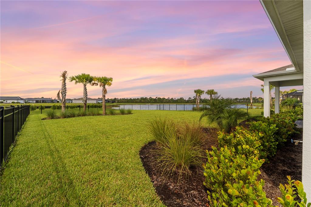 A grassy backyard with palm trees and a black fence overlooks a pond at sunset — 44363 KELLY DRIVE, PUNTA GORDA, FL