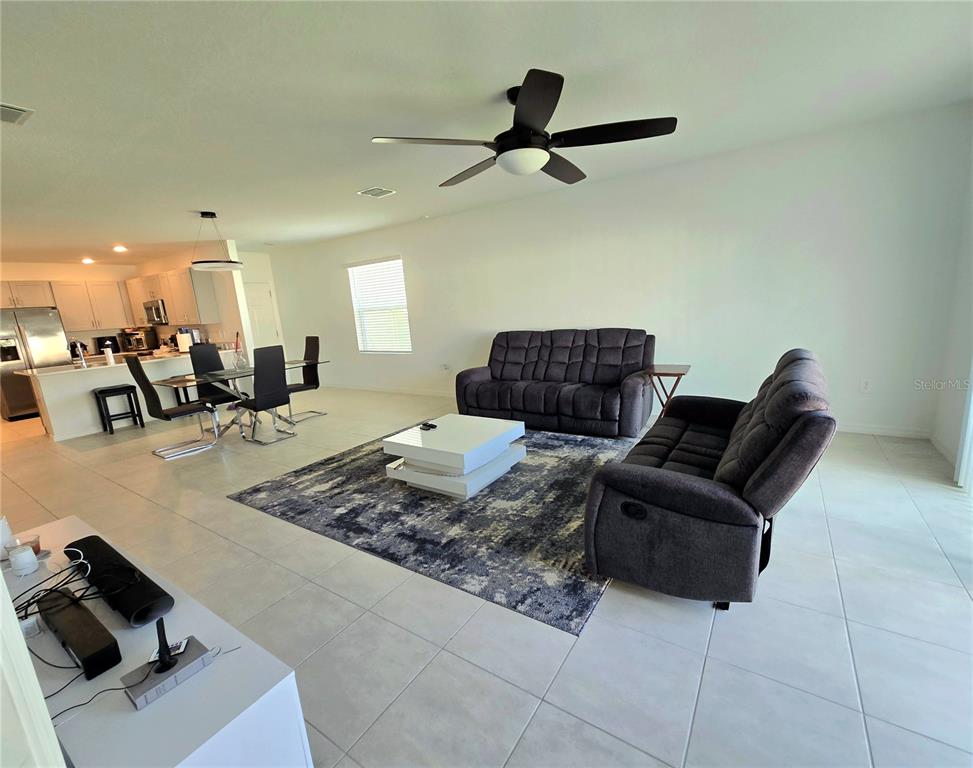 An open-concept living room features tile flooring, a dark sofa set, and a dining area — 357 WAYLAND DRIVE, HAINES CITY, FL