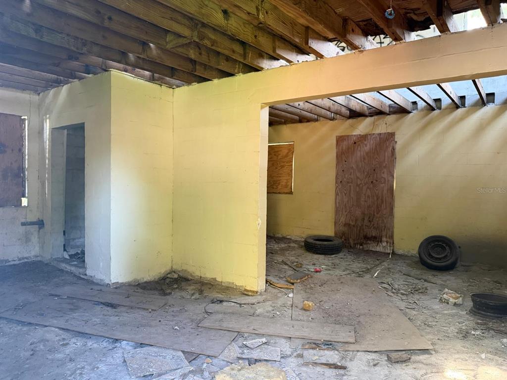 An unfinished room with exposed ceiling joists, yellow concrete block walls, and debris-covered floors — 375 TRAILER LANE, KISSIMMEE, FL
