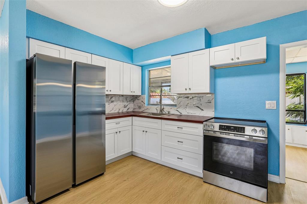 A kitchen features white cabinets, a stainless steel refrigerator, and dark wood countertops — 104 E GRAPEFRUIT CIRCLE, CLEARWATER, FL