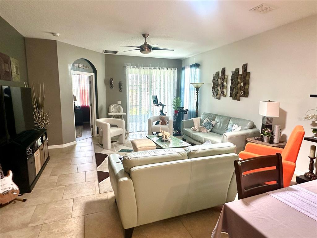 A living room features tile flooring, two light-colored sofas, an orange armchair, and a ceiling fan — 16484 CENTIPEDE STREET, CLERMONT, FL