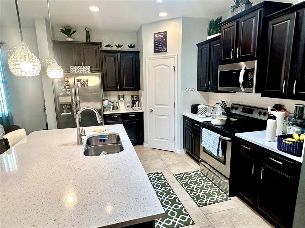 A kitchen features dark wood cabinets, stainless steel appliances, and a large white quartz island — 16484 CENTIPEDE STREET, CLERMONT, FL