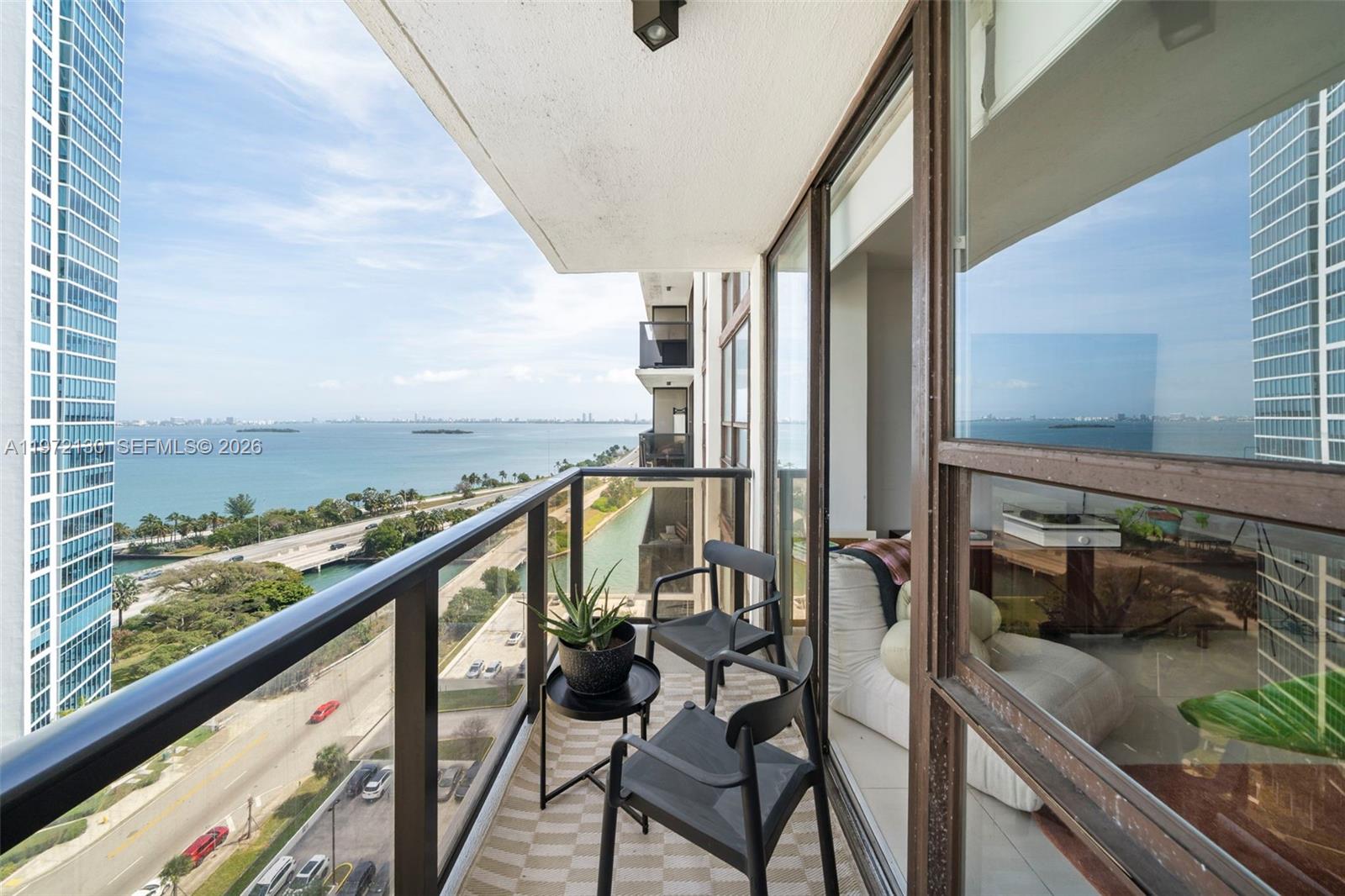 A balcony with two chairs and a small table overlooks a bay and highway — 600 NE 36th St # 1815, Miami FL 33137, MIAMI, FL
