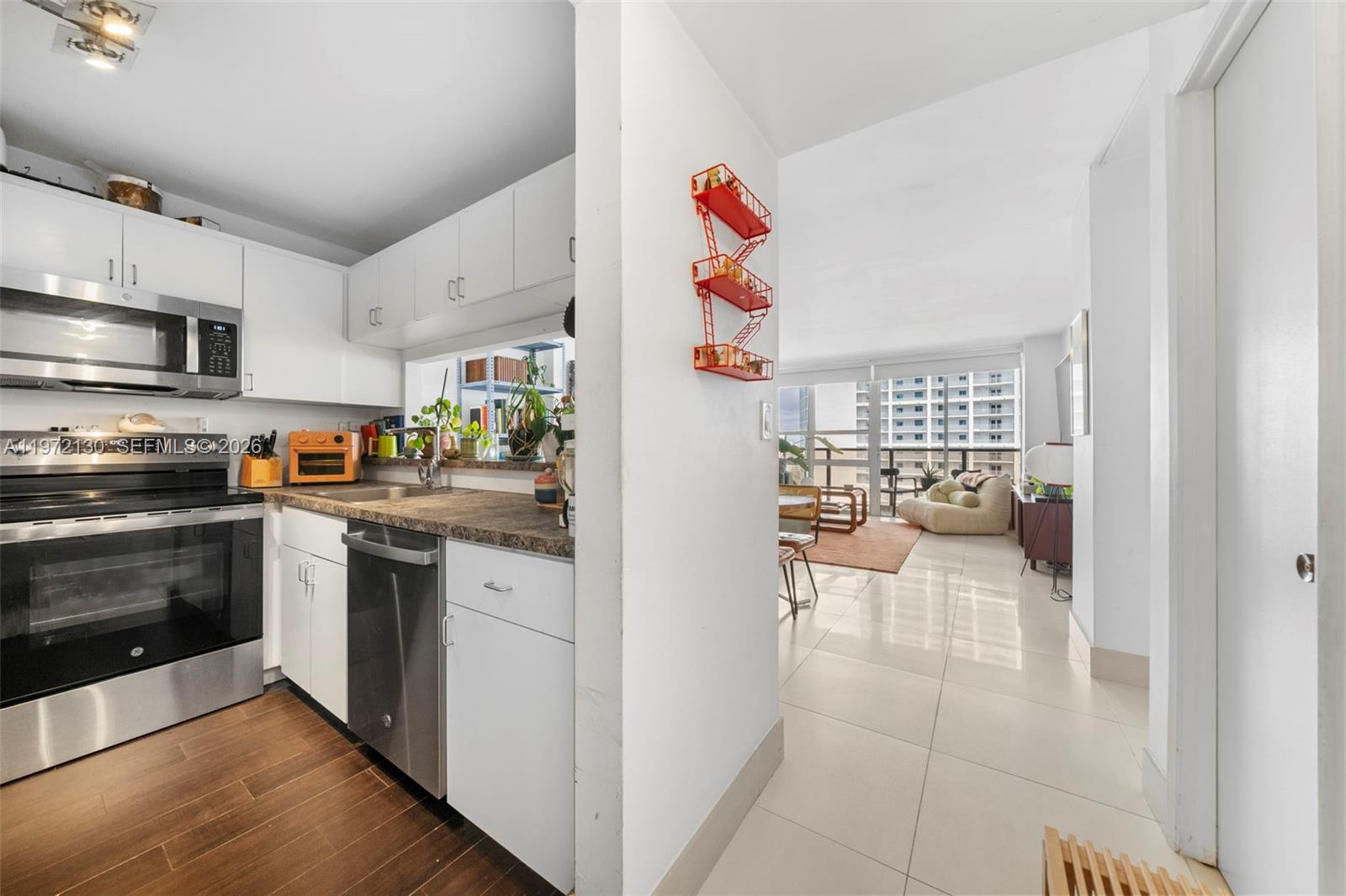 A kitchen with white cabinets and stainless steel appliances opens into a bright living area — 600 NE 36th St # 1815, Miami FL 33137, MIAMI, FL