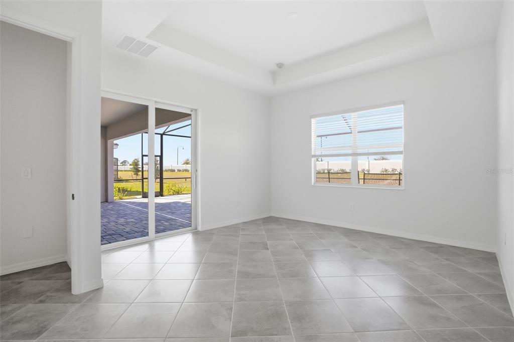 An empty room with gray tile flooring, a tray ceiling, and sliding glass patio doors — 19715 TROUT TERRACE, LAKEWOOD RANCH, FL