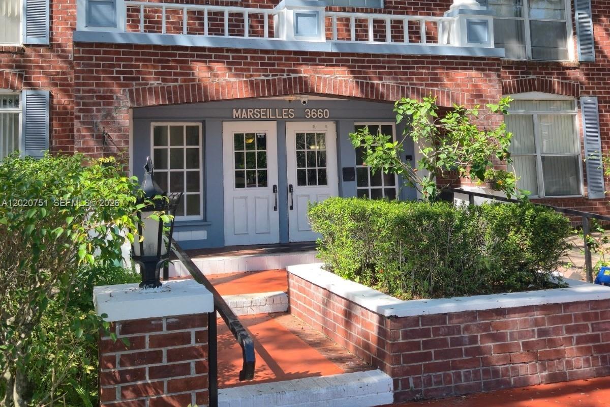 The exterior of a brick building features a double-door entrance with a white railing above — LAUDERHILL, FL