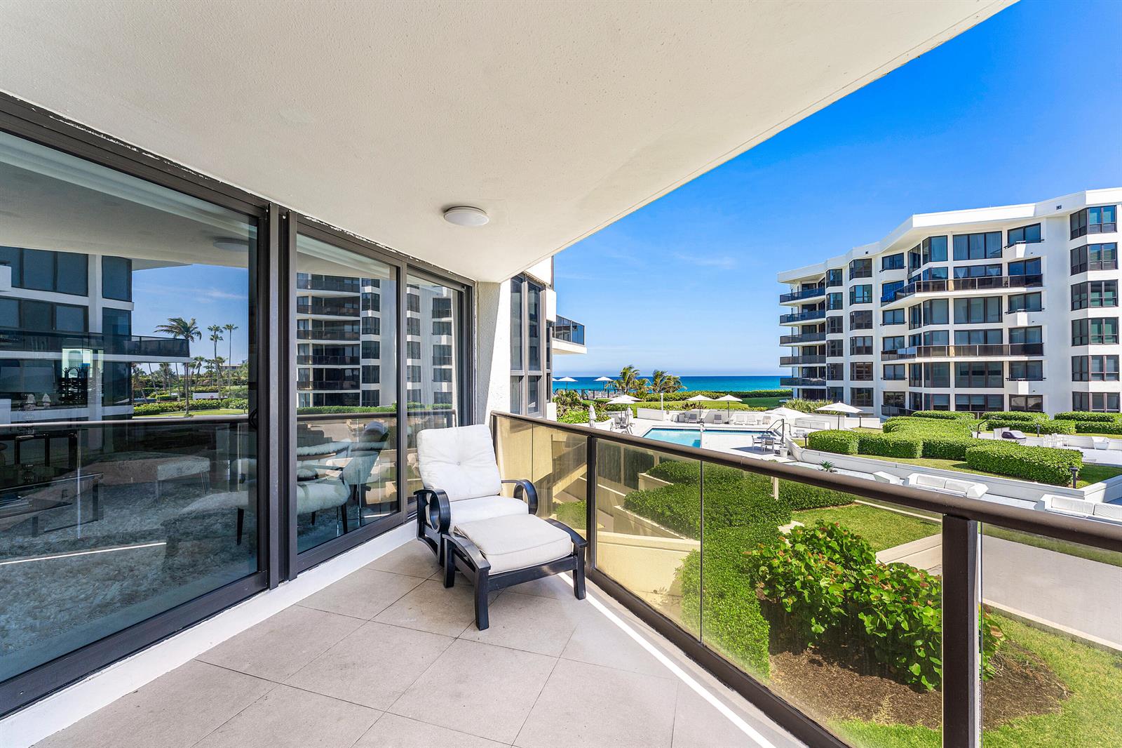 A balcony with a lounge chair overlooks a swimming pool, landscaped grounds, and the ocean — 3120 S Ocean Boulevard # 202, Palm Beach FL 33480, PALM BEACH, FL