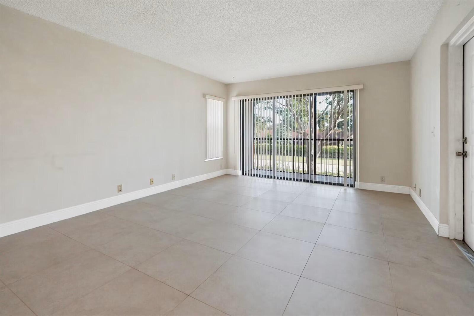An empty living room features light-colored walls, large floor tiles, and a sliding glass door — 802 Sky Pine Way # E2, FL 33415, FL