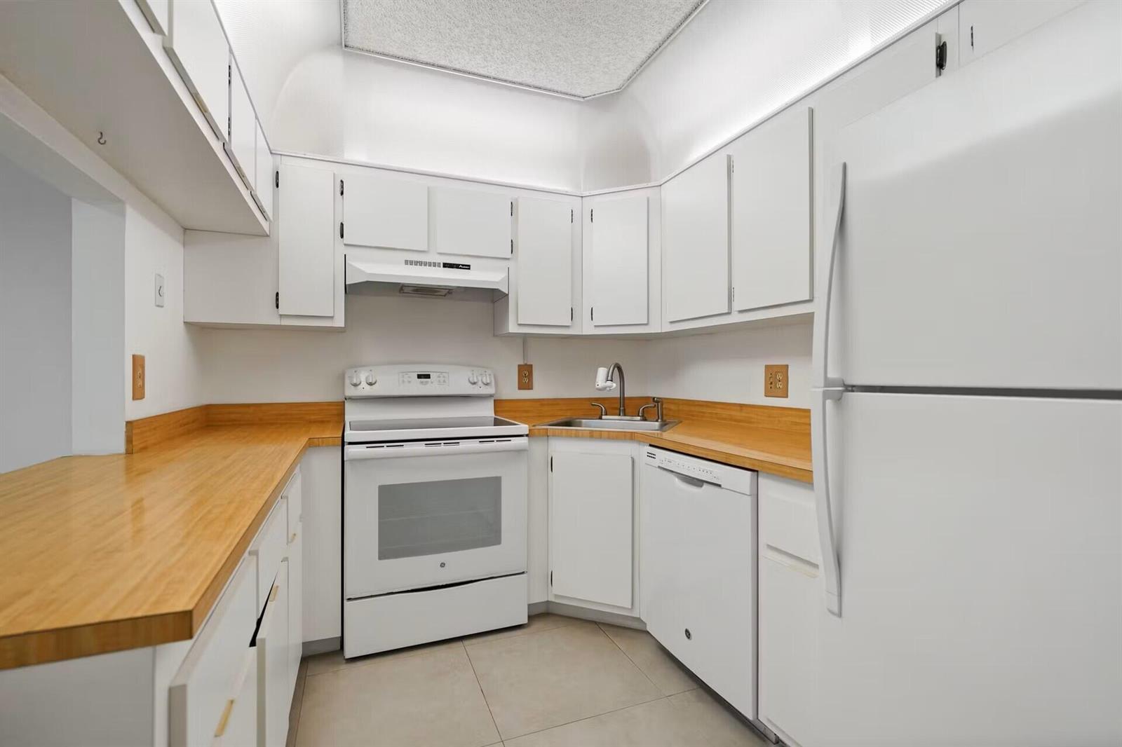 A small kitchen features white cabinets, light wood countertops, and white appliances — 802 Sky Pine Way # E2, FL 33415, FL