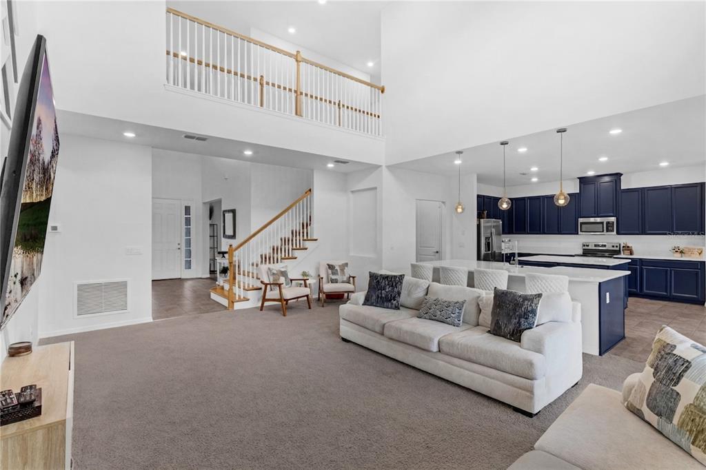 A spacious living room with high ceilings, gray carpet, and an open kitchen with blue cabinets — 2901 AGOSTINO TERRACE, KISSIMMEE, FL
