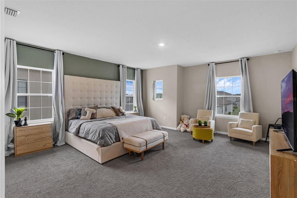A spacious bedroom features a tufted headboard, gray carpet, and two armchairs near a window — 2901 AGOSTINO TERRACE, KISSIMMEE, FL