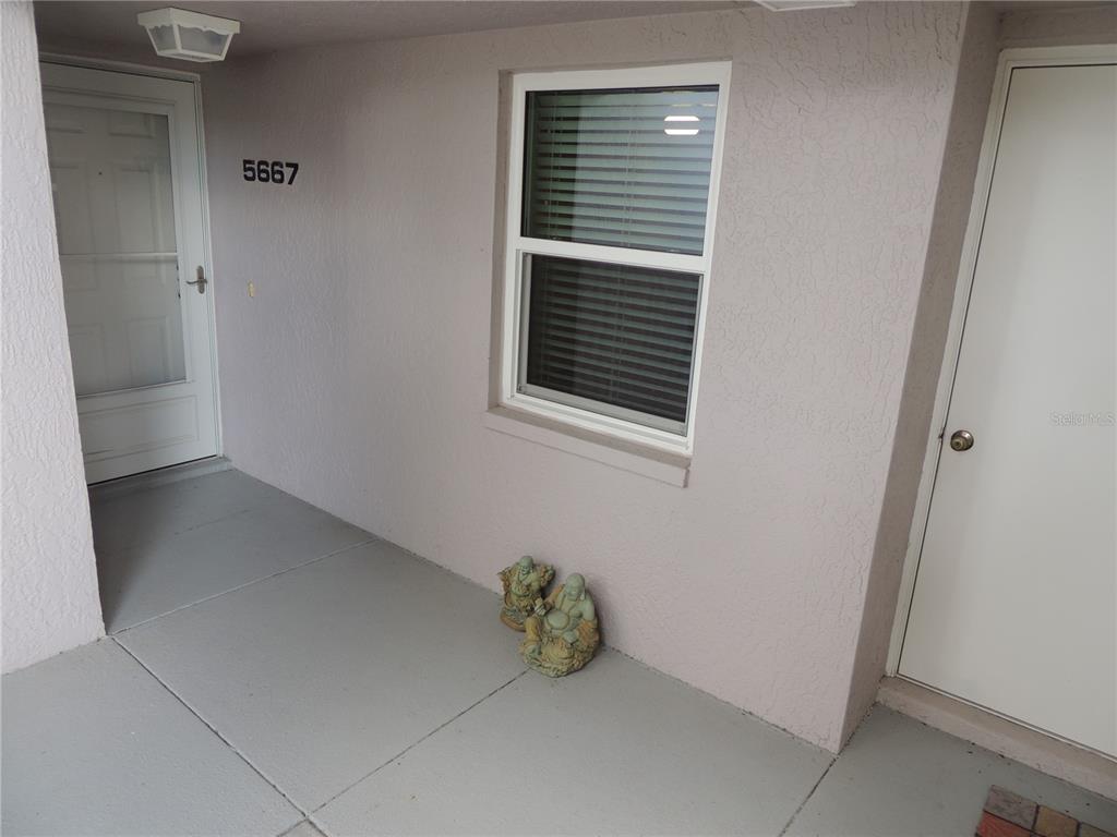A covered entryway features a white door, a window with blinds, and two small statues — 5667 SHEFFIELD GREENE CIRCLE UNIT 59, SARASOTA, FL