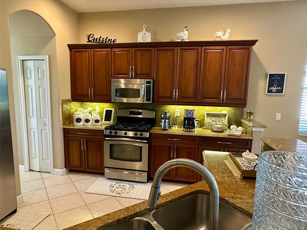 A kitchen features wooden cabinets, granite countertops, stainless steel appliances, and a tiled floor — 137 MEDICI TERRACE, NORTH VENICE, FL