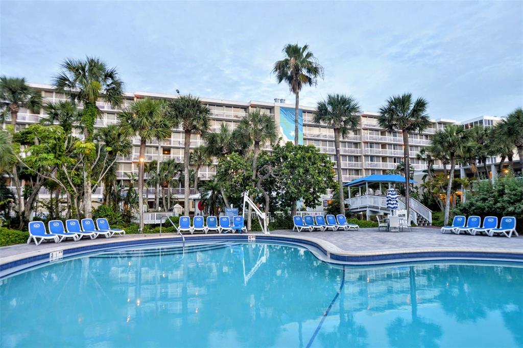 A large swimming pool sits in front of a multi-story hotel with palm trees — 5500 GULF BOULEVARD UNIT 7230, ST PETE BEACH, FL