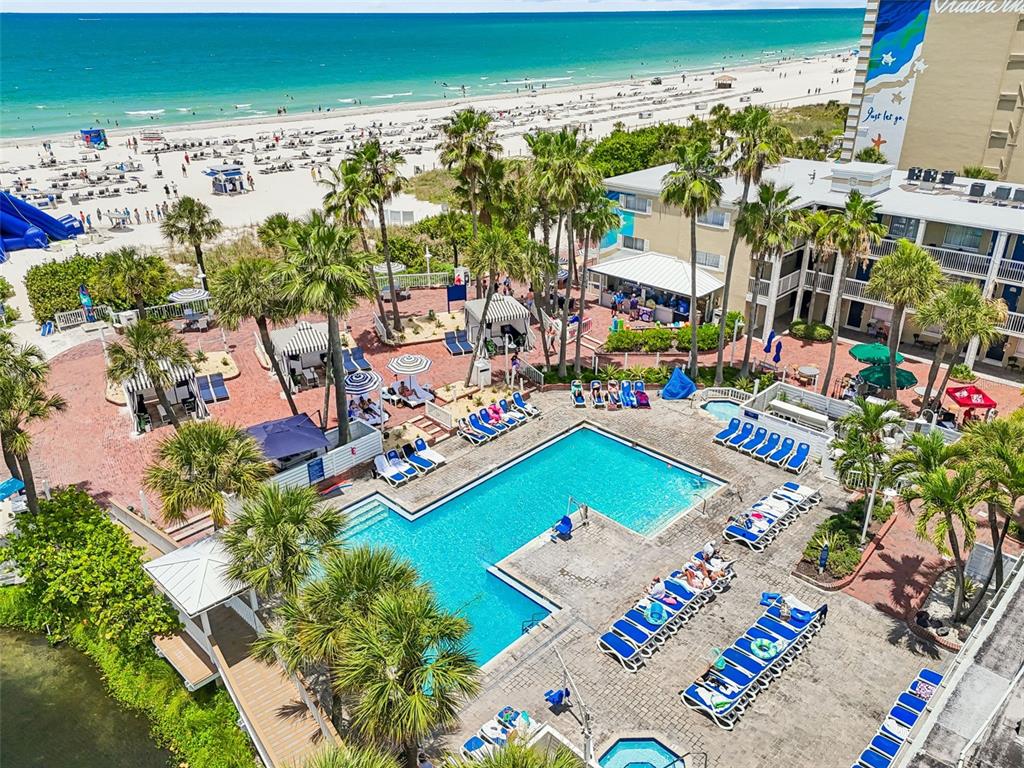 An aerial view shows a resort swimming pool, palm trees, and a beach with ocean — 5500 GULF BOULEVARD UNIT 7230, ST PETE BEACH, FL