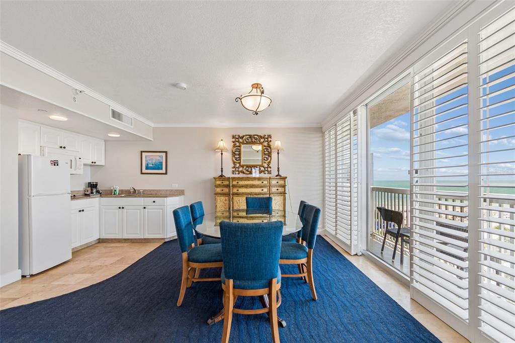 A dining area with blue chairs and a rug sits next to a small kitchen — 5500 GULF BOULEVARD UNIT 7230, ST PETE BEACH, FL