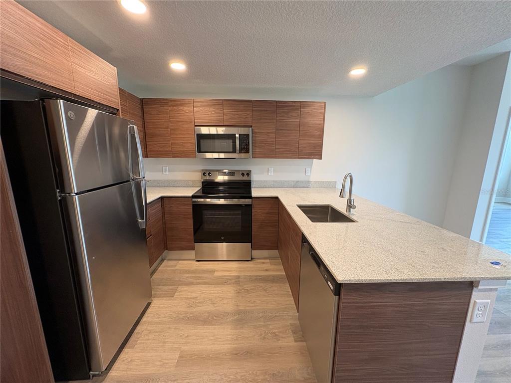 A modern kitchen features wood-grain cabinets, stainless steel appliances, and a granite-topped island — 4424 S TEXAS AVENUE UNIT 1-118, ORLANDO, FL