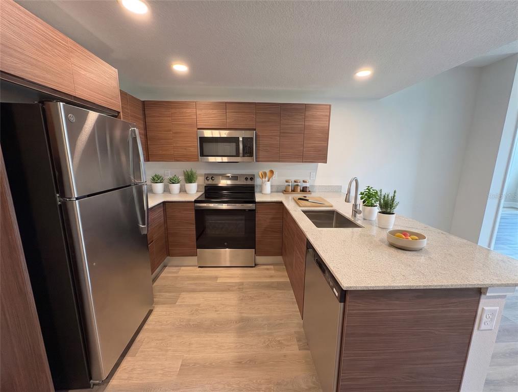 A modern kitchen features wood-grain cabinets, stainless steel appliances, and a light-colored stone countertop — 4424 S TEXAS AVENUE UNIT 1-118, ORLANDO, FL