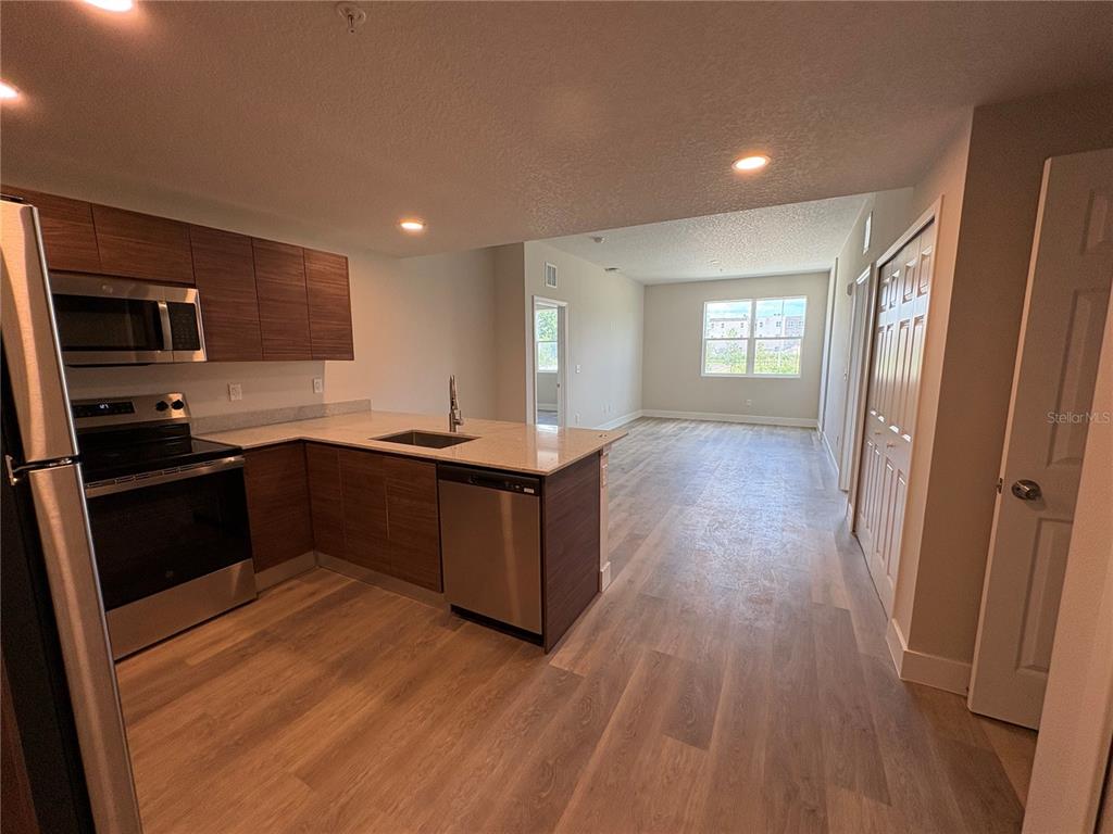 A kitchen with wood-tone cabinets and stainless steel appliances opens into a living area — 4424 S TEXAS AVENUE UNIT 1-118, ORLANDO, FL