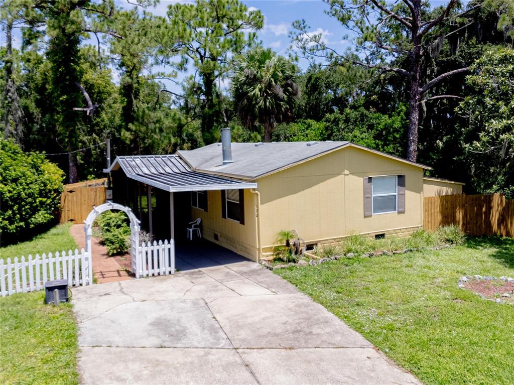 A yellow single-story house features a metal carport, a white picket fence, and surrounding trees — 120 NIVER STREET, PORT ORANGE, FL