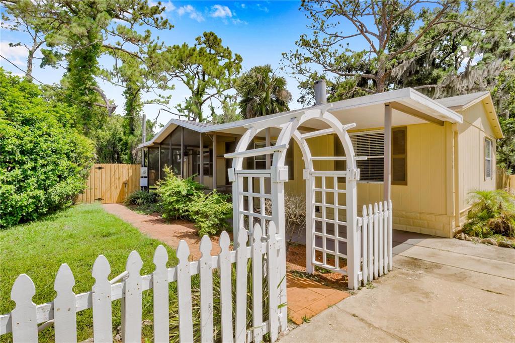 A yellow mobile home features a white picket fence, a garden arbor, and a screened porch — 120 NIVER STREET, PORT ORANGE, FL