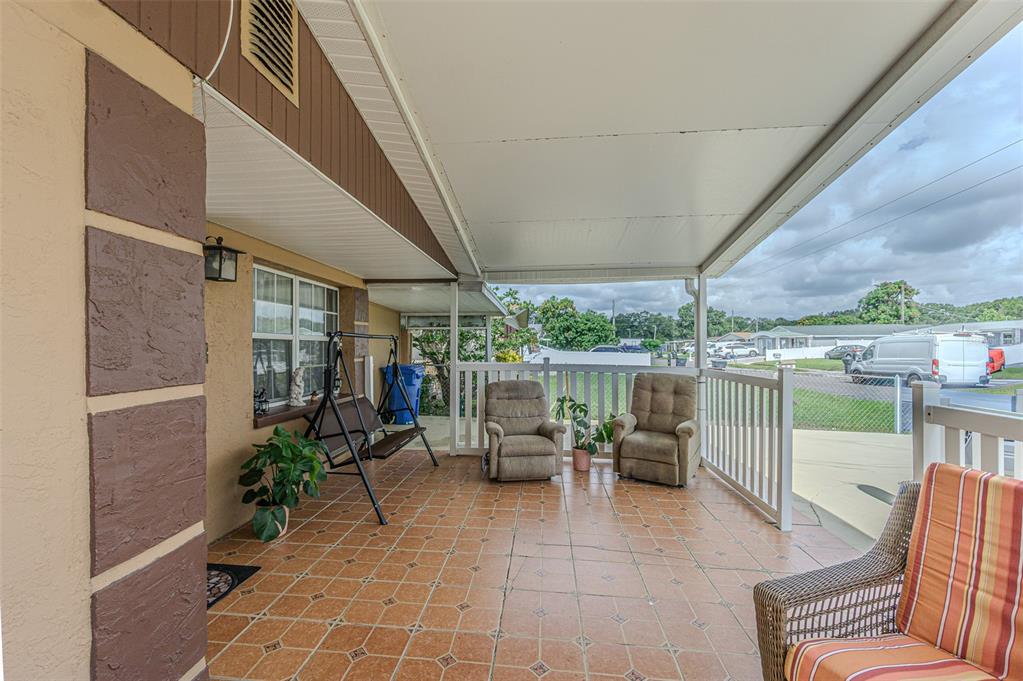 A covered patio features tiled flooring, a porch swing, two recliners, and a wicker chair — 4536 W IDLEWILD AVENUE, TAMPA, FL