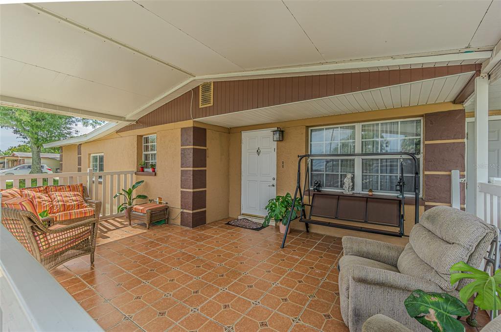 A covered porch features tiled flooring, a white front door, and various outdoor seating options — 4536 W IDLEWILD AVENUE, TAMPA, FL
