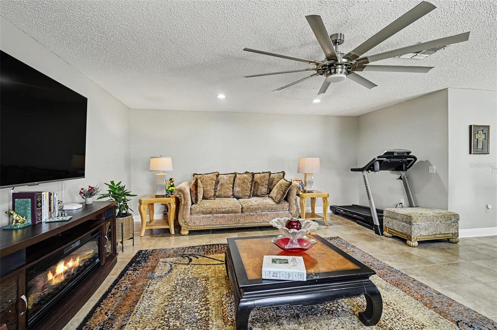 A living room features a sofa, coffee table, fireplace console, treadmill, and a ceiling fan — 121 MAYFIELD DRIVE, SANFORD, FL