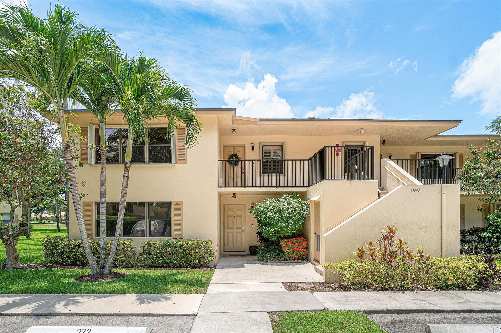 A two-story tan apartment building features a palm tree, a balcony, and a concrete walkway — 2898 SW 22nd Circle # 232a, Delray Beach FL 33445, DELRAY BEACH, FL