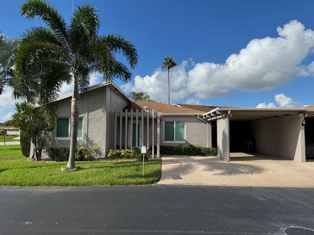 A single-story house with a carport, palm tree, and gray stucco exterior under blue skies — 14747 Wildflower Lane, Delray Beach FL 33446, DELRAY BEACH, FL